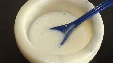Eine cremige Gesichtsmaske aus Quark wird mit einem blauen Löffel in einer weißen Schüssel angerührt, vorbereitet für die Anwendung.