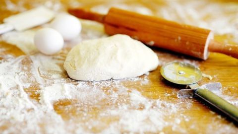 Der Pizzateig liegt auf einer bemehlten Arbeitsfläche, während neben ihm ein Nudelholz und Eier vorbereitet werden.