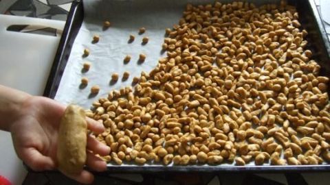 Eine Hand formt ein Hundeleckerli, während eine Backblech mit goldbraunen, selbstgemachten Hundeleckerlis auf einem Tisch liegt.