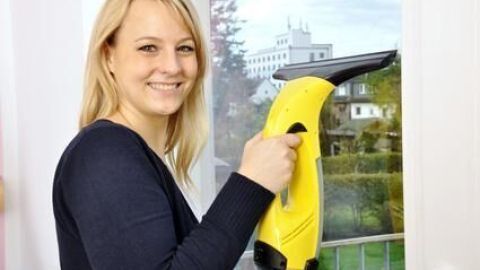 Eine Frau reinigt mit einem Kärcher Fenstersauger das Fliegengitter an einem Fenster in einem hellen Raum.