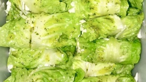 Chinakohlröllchen liegen ordentlich in einer Schale und sind mit einer würzigen Füllung gefüllt, auf einer weißen Unterlage.