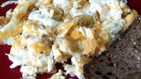 Rührei liegt appetitlich auf einem roten Teller, während eine Scheibe Brot daneben liegt, ideal für ein herzhaftes Frühstück.