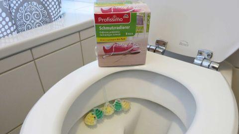Ein Schmutzradierer liegt auf einem Toilettenrand, während bunte Reinigungsschwämme im WC schwimmen, um Urinstein zu entfernen.