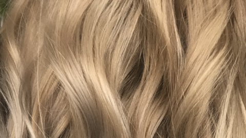 Lange, wellige Haare in sanften, natürlichen Farbtönen leuchten im Sonnenlicht, während die Person entspannt steht.