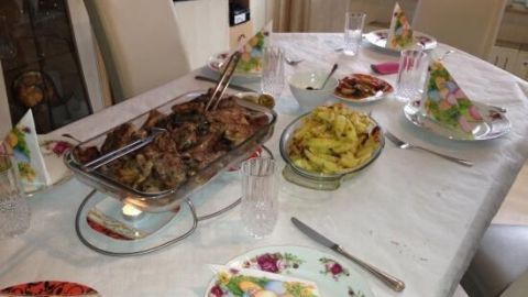 Ein Tisch ist reich gedeckt mit original griechischem Gyros, Beilagen und verschiedenen Saucen, umgeben von Stühlen und einer freundlichen Atmosphäre.
