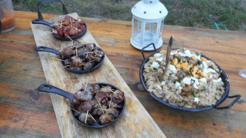 Aprikosen mit Bacon liegen auf einer Holzplatte, daneben eine Laterne, umgeben von einer natürlichen Umgebung.