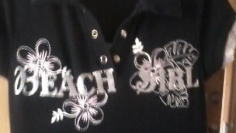 Ein schwarzes T-Shirt hängt an einem Kleiderbügel, mit floralem Motiv und dem Schriftzug "BEACH GIRL".