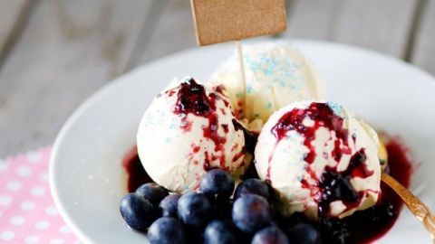 Eis serviert mit Blaubeeren und roter Soße auf einem Teller. Ein Schild mit „mit LIEBE gemacht“ steht darauf.