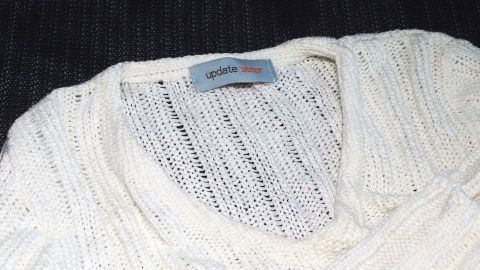 Ein weißer Pullover mit einem weiten Ausschnitt liegt auf einem dunklen Hintergrund. Die Struktur ist grob und gestrickt.