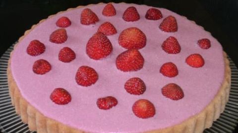 Ein Erdbeerkuchen mit Erdbeerpüree ist auf einem eleganten Untersetzer platziert. Saftige Erdbeeren zieren die rosa Oberfläche.