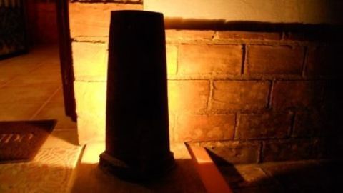 Ein schwarzer Dachziegel steht auf einem Boden und strahlt warmes Licht aus, während er vor einer gemauerten Wand platziert ist.