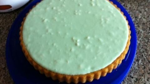 Ein runder Hexenkuchen mit grüner Glasur sitzt auf einer blauen Platte auf einer Küchenarbeitsplatte.