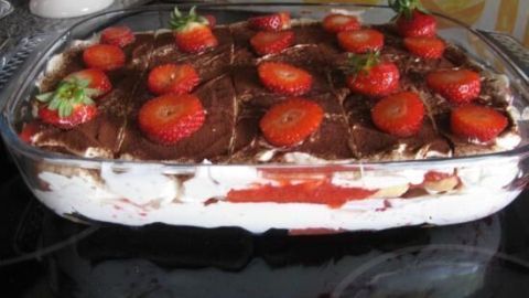 Ein erfrischendes Erdbeer Tiramisu liegt in einer Glasform, mit saftigen Erdbeeren dekoriert und in einer Küche platziert.