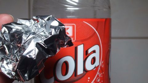 Ein Hand hält eine zerknüllte Alufolie, während sie in der Nähe einer Cola-Flasche steht. Das Chrom polieren zeigt innovative Methoden.