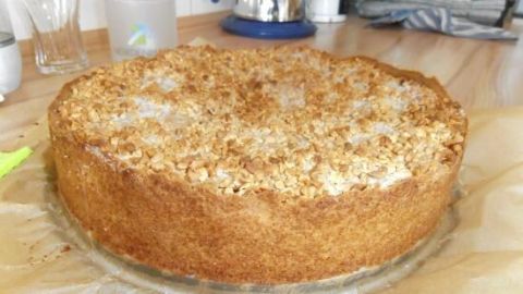 Ein Apfelkuchen mit Krokant steht auf einem Tisch, umgeben von Küchenutensilien, und glänzt verlockend.