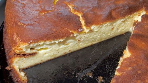 Ein goldbrauner Käsekuchen ohne Boden wird gerade angeschnitten, um ein Stück daraus zu servieren.