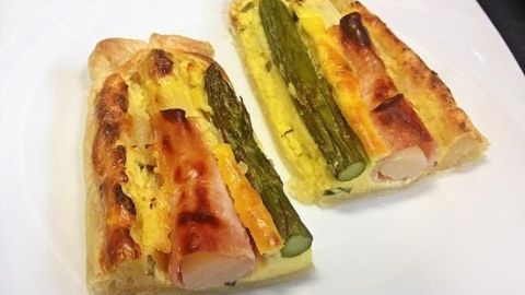 Zwei Stücke Spargel-Tarte mit Schinken liegen auf einem weißen Teller, goldbraun gebacken und appetitlich angerichtet.