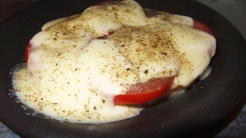 Ein appetitliches Baguette mit geschmolzenem Mozzarella und frischen Tomaten wird in einer schwarzen Schale serviert.