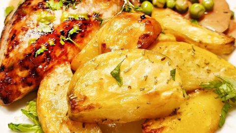 Geröstete Knoblauch-Ofenkartoffeln liegen neben saftigem Hähnchen, garniert mit frischen Kräutern und farbenfrohem Gemüse.