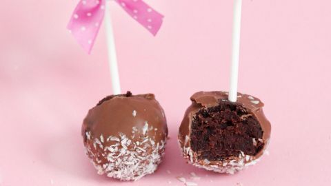 Schokoladenmilka-Balls stehen auf einem rosa Hintergrund, dekoriert mit rosa Schleifen, einer ist angerissen.