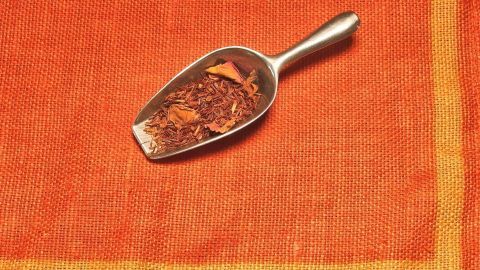 Ein metallischer Löffel mit duftenden Gewürzen liegt auf einem orangefarbenen Tuch, das den Raum mit Aroma füllt.