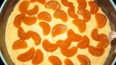 Ein Mohnkuchen mit einer obersten Schicht aus Mandarinenstücken in einer runden Form wird in einer Küche präsentiert.