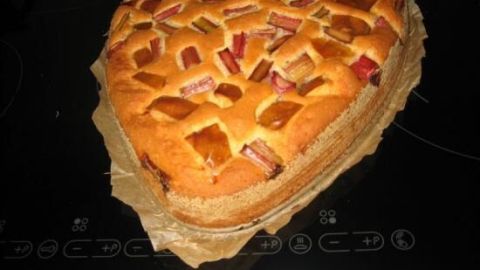 Ein herzförmiger Kuchen ohne Ei liegt auf einem Backblech und ist mit Fruchtstücken belegt, frisch aus dem Ofen.