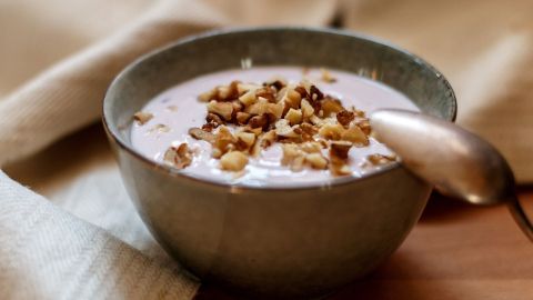 In einer Schüssel liegt cremiges Joghurt, das mit Nüssen garniert ist, auf einem Holztisch in einer gemütlichen Umgebung.