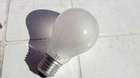 Eine Glühbirne liegt auf einer weißen Oberfläche, bereit zum Austauschen, während ihr Schatten darunter sichtbar ist.