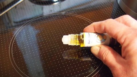Ein Hand hält eine Flasche ätherisches Öl, während es auf ein Kochfeld aufgetragen wird, um unangenehme Kochgerüche zu beseitigen.