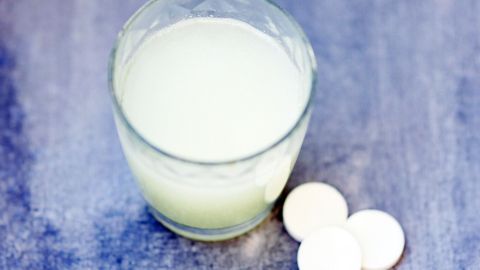 Ein Glas mit einer trüben Flüssigkeit steht neben drei Tabletten. Die Szene vermittelt eine Verbindung zu Magnesium bei Zähneknirschen.