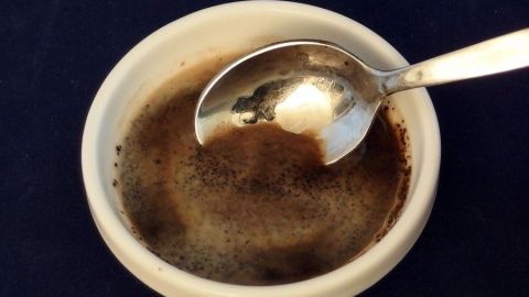 Eine Schüssel mit Kaffeesatz steht auf einem dunkelblauen Untergrund, während ein Löffel darin verweilt, bereit zur Anwendung.