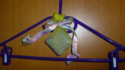 Netz aus Obst hängt gefüllt an einem violetten Kleiderbügel mit buntem Band, vor einem Holzschrank.