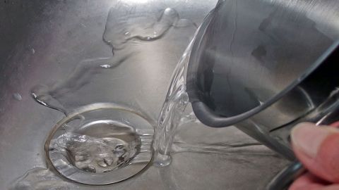 Heißes Wasser und Spülmittel kann - regelmäßig angewendet - helfen, den Abfluss freizuhalten. Wasser wird aus einem Behälter in ein Spülbecken gegossen, das einen verstopften Abfluss hat, um die Verstopfung zu lösen.