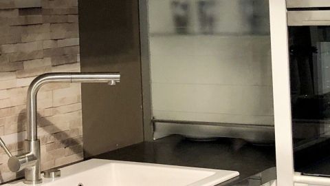 Eine Emaille-Spüle steht auf einem dunklen Arbeitsbereich, während im Hintergrund eine moderne Kücheneinrichtung sichtbar ist.