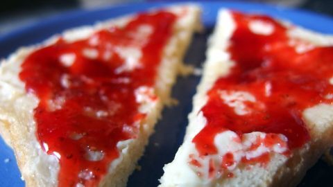 Auf zwei Brotscheiben liegt leuchtend rote Erdbeermarmelade, serviert auf einem blauen Teller.