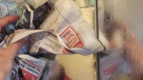 Eine Person hält zerknülltes Papier in der Hand und reinigt einen beschlagenen Spiegel im Badezimmer.
