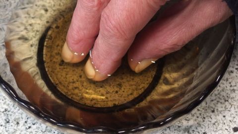 Ein Hand, die mit fingernägeln in eine Schale mit Olivenöl eintaucht, um feste Fingernägel zu erzielen.