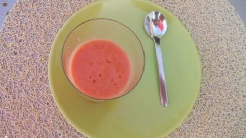 Eine Schüssel mit Salmorejo Cordobes, einer kalten Tomatencreme, steht auf einem grünen Teller neben einem Löffel auf einem Tisch.