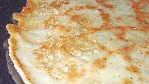 Ein goldbrauner Pfannkuchen liegt auf einer heißen Pfanne, bereit zum Servieren. Der Pfannkuchen exhibiert knusprige Ränder.