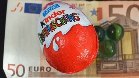 Ein Überraschungsei liegt auf einem 50-Euro-Schein, umgeben von einigen grünen Murmeln, symbolisiert ein Geldgeschenk.