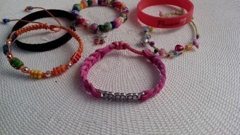 Armbänder liegen dekorativ auf einem weißen Tischläufer, darunter ein pinkes mit der Gravur "Hope", welche an Urlaub erinnern.