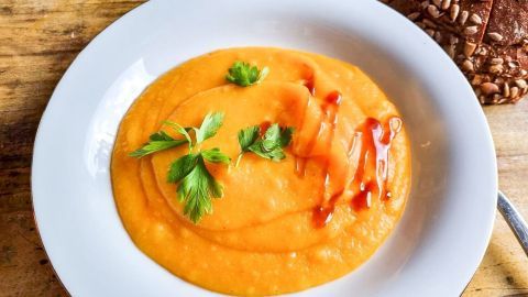 Eine cremige Suppe aus roten Linsen und Karotten wird in einer weißen Schale serviert, garniert mit frischer Petersilie.
