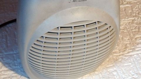 Ein Ventilator sorgt für kühlende Luftzirkulation auf einem Schreibtisch in einem hellen, warmen Raum im Hochsommer.