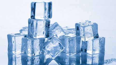 Durchsichtige Eiswürfel liegen in verschiedenen Höhen auf einer glatten Oberfläche, umgeben von leichtem Blau, das Frische vermittelt.