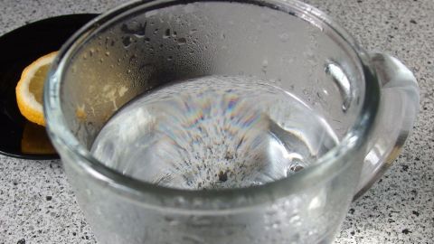 Ein Glas heißes Wasser steht auf einem Tisch, während es dampft. Nebenbei liegt eine Zitronenscheibe.