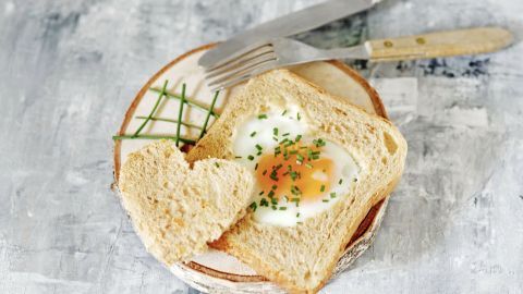Ein herzförmiges Stück Toast mit einem Spiegelei liegt auf einem Teller, mit einem Besteck neben dem Gericht.