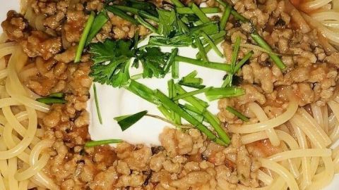 Ein Teller Spaghetti mit Bolognese-Sauce, garniert mit frischem Koriander und einem Klecks Creme, wirkt appetitlich.