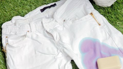 Weiße Jeans mit Pflanzenfleck liegen auf grünem Gras, daneben steht ein Stück Seife für die Fleckenentfernung.