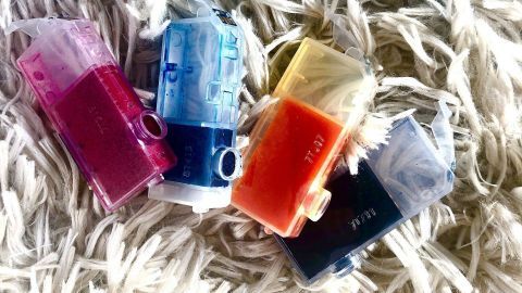Lila, blaue, orange und schwarze Druckertintenpatronen liegen unordentlich auf einem weißen, flauschigen Teppich.
